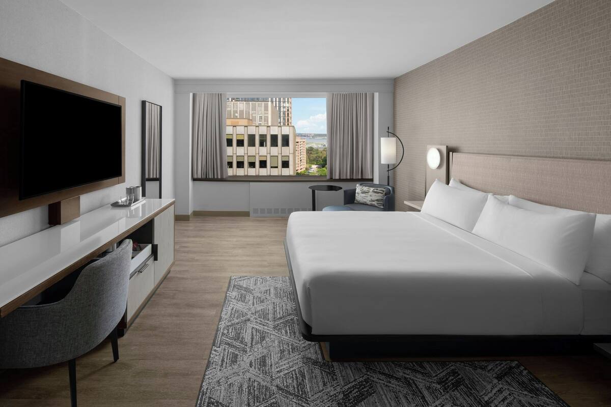 A modern hotel room with a large bed, a TV, a desk, and a view of the city.