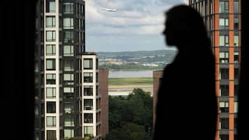 Un edificio de gran altura con varios pisos y grandes ventanales, con vista a una masa de agua y un avión distante.