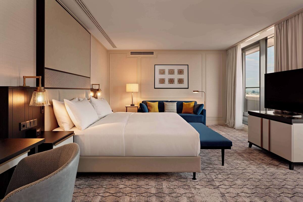 A hotel room with a large bed, a sofa, a desk, a TV, and a city view.