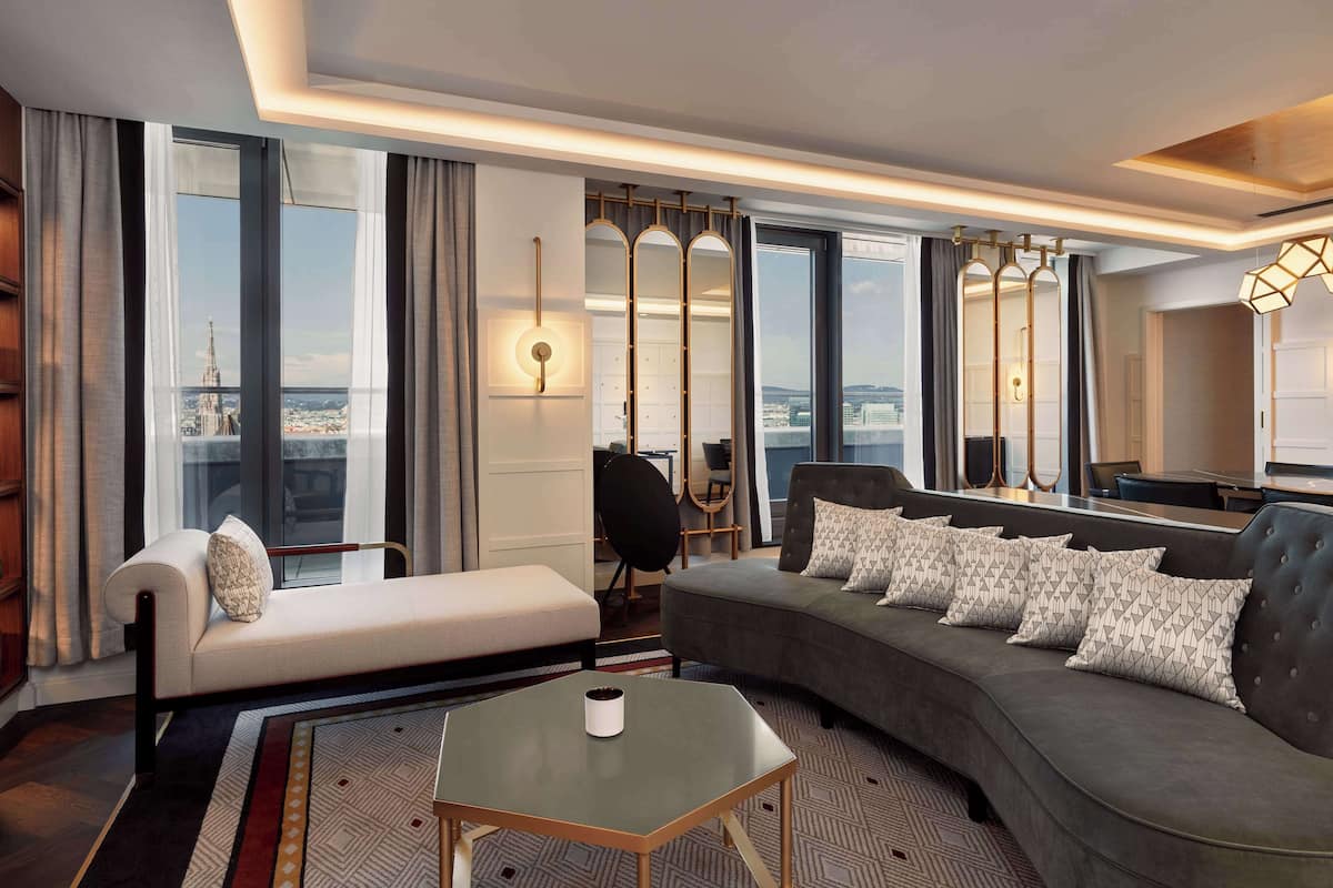 A modern hotel room with a sofa, a small table, and a large window offering a city view.