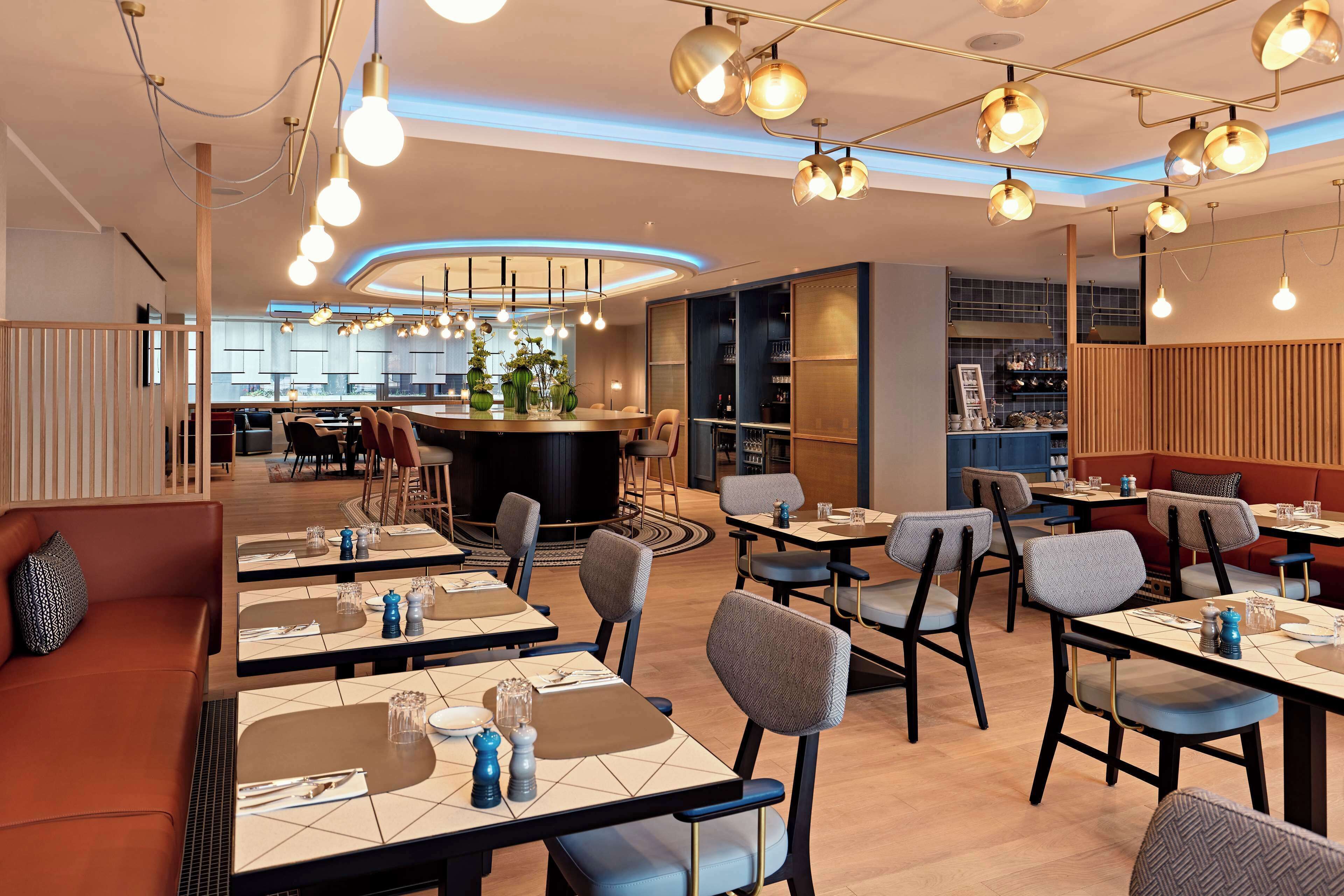 Un interno ristorante moderno con diversi tavoli, sedie e lampade a sospensione.