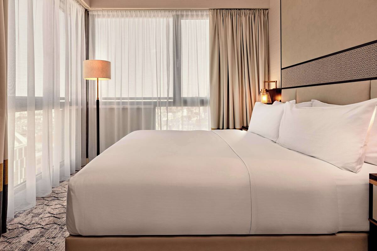A hotel room with a large bed, a bedside lamp, and sheer curtains.