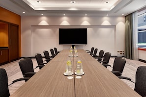 A conference room with a long table, chairs, a flat-screen TV, and a projector screen. - Hilton Vienna Park (Vienna)