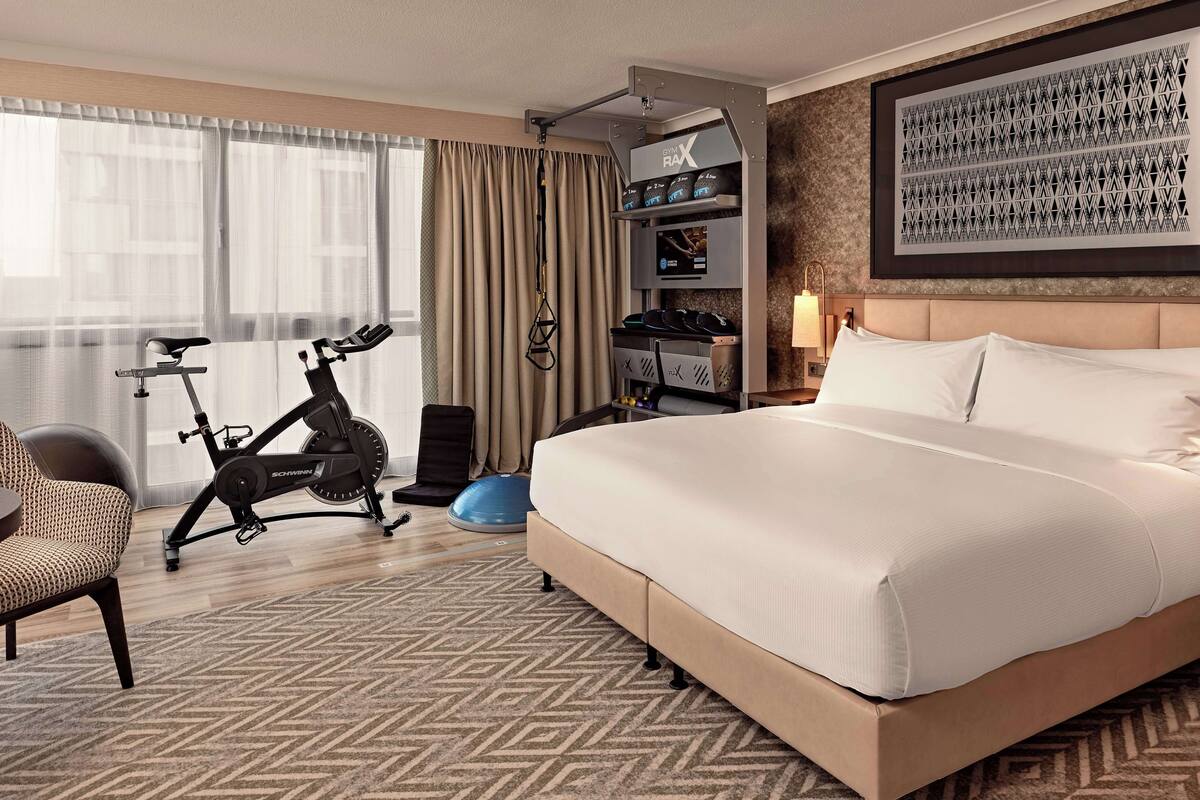 A hotel room with a bed, exercise bike, and a wall-mounted TV.