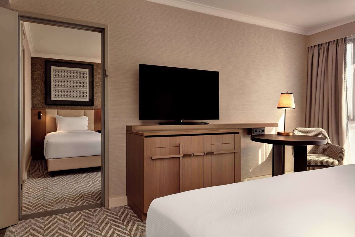A hotel room with a bed, a television, a desk with a lamp, and a chair.