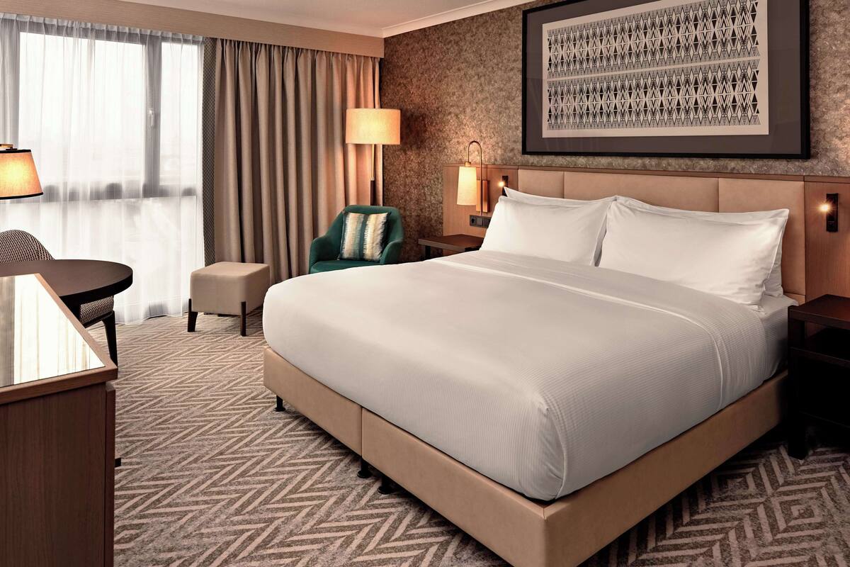 A hotel room with a large bed, a desk, a chair, and a lamp.