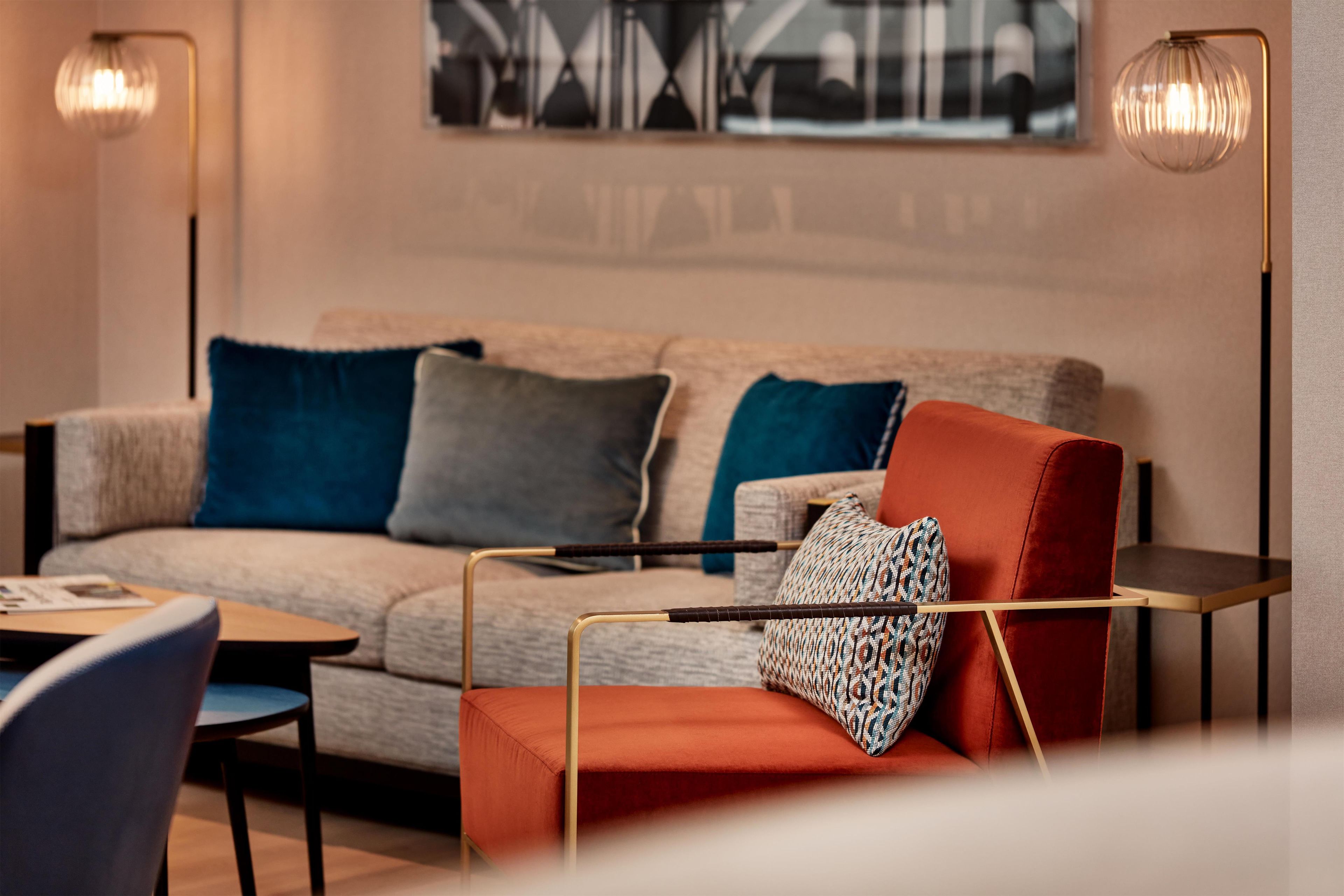 A modern living room with a sofa, a coffee table, and a chair. There is a painting on the wall and two lamps on either side of the sofa.