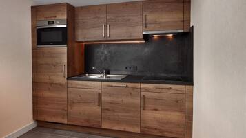 Eine kleine Küche mit Holzausstattung, einem eingebauten Backofen und einer Spüle aus Edelstahl.