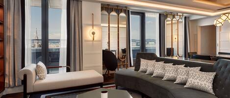A modern hotel room with a sofa, a small table, and a view of the cityscape through large windows.