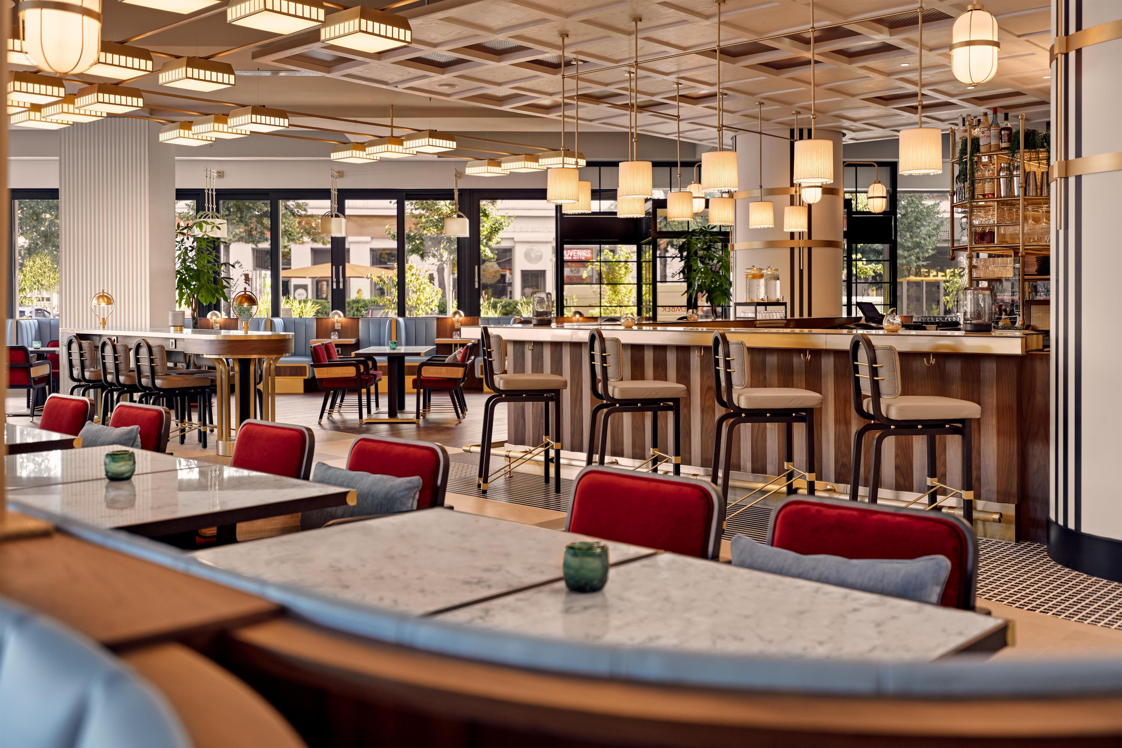 En modern restauranginteriör med högt i tak, hängande lampor och en blandning av olika sittarrangemang, inklusive bord och barstolar.