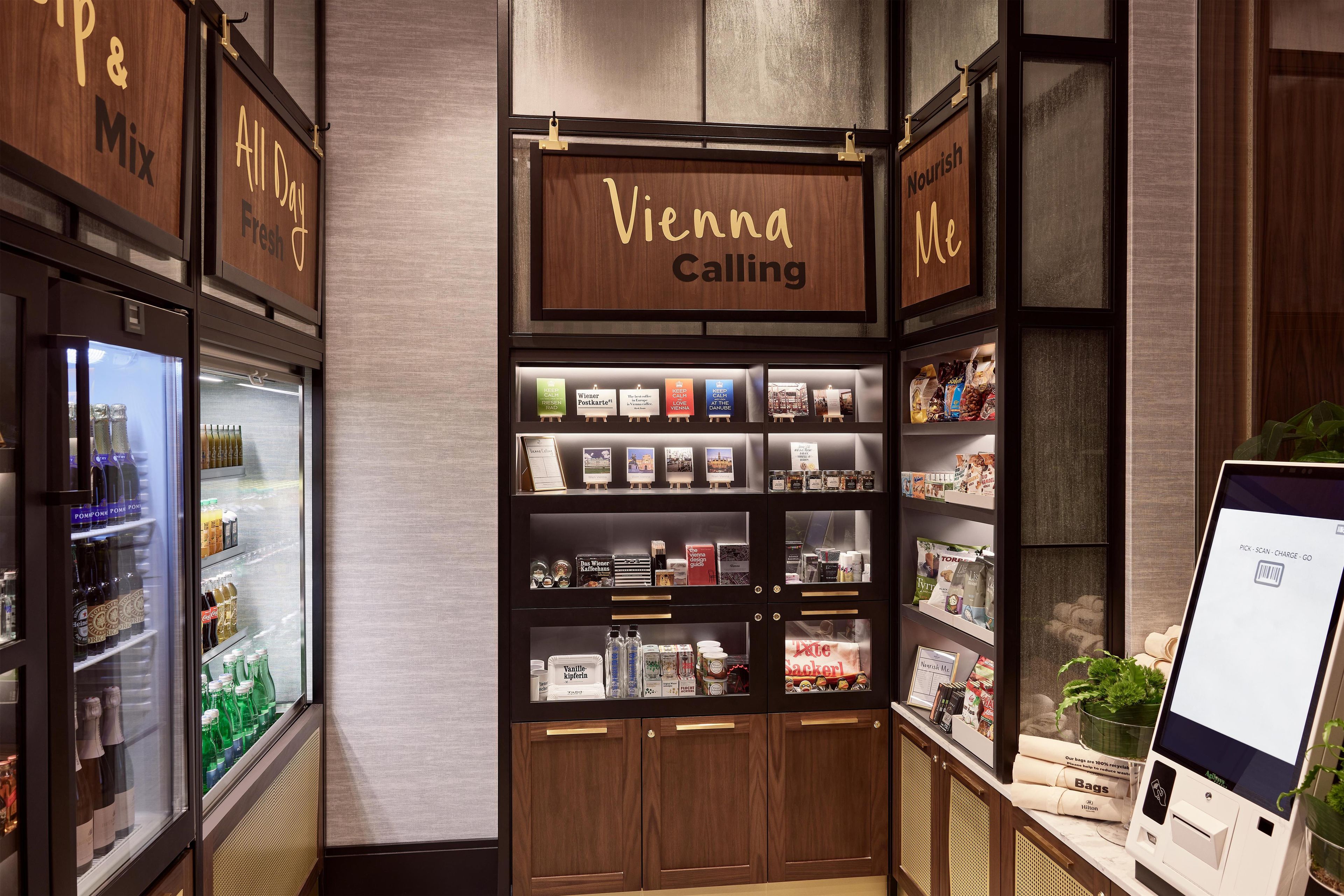 A hotel lobby with a minibar, a Vienna Calling sign, and a self-service kiosk.