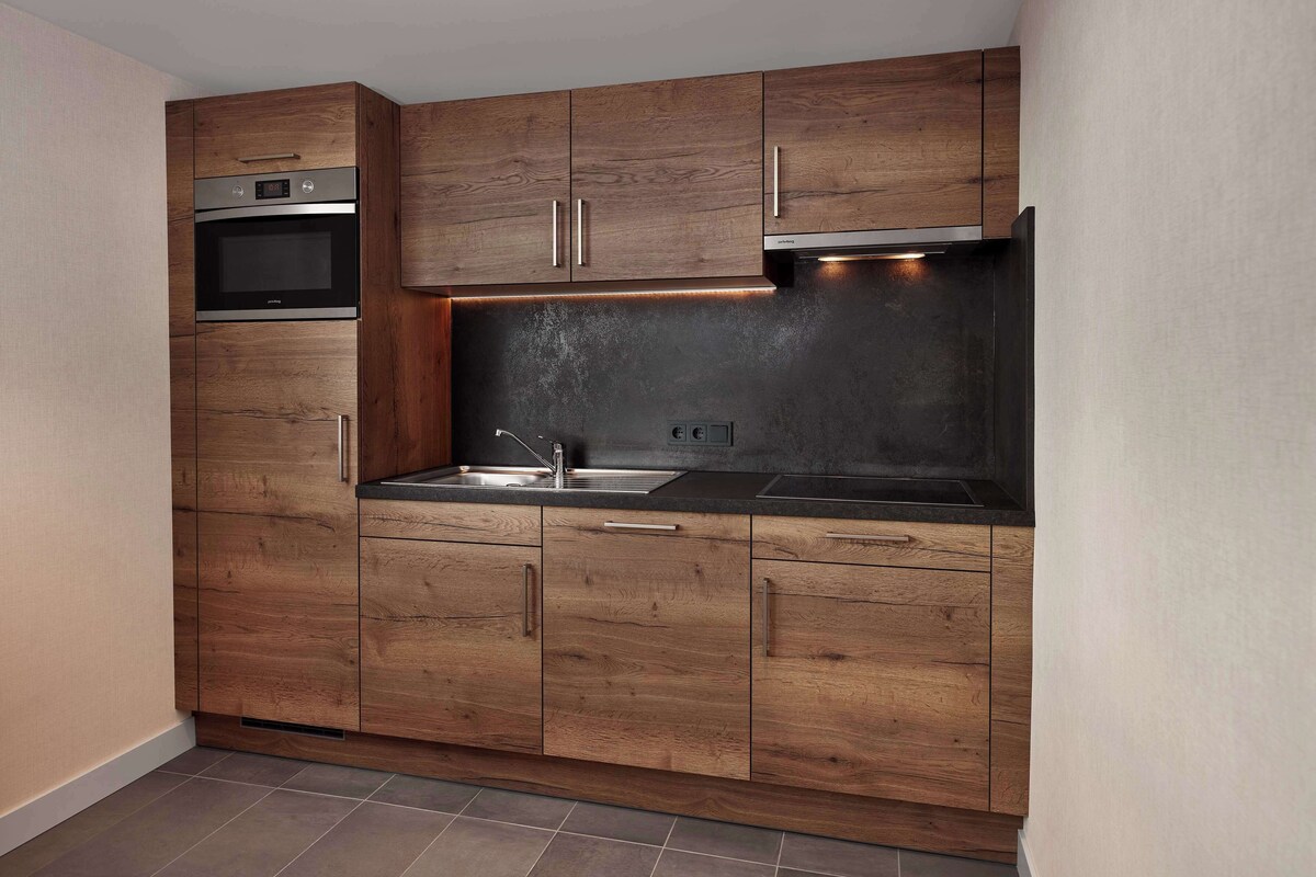 A modern kitchen with wooden cabinetry, stainless steel appliances, and a black countertop.