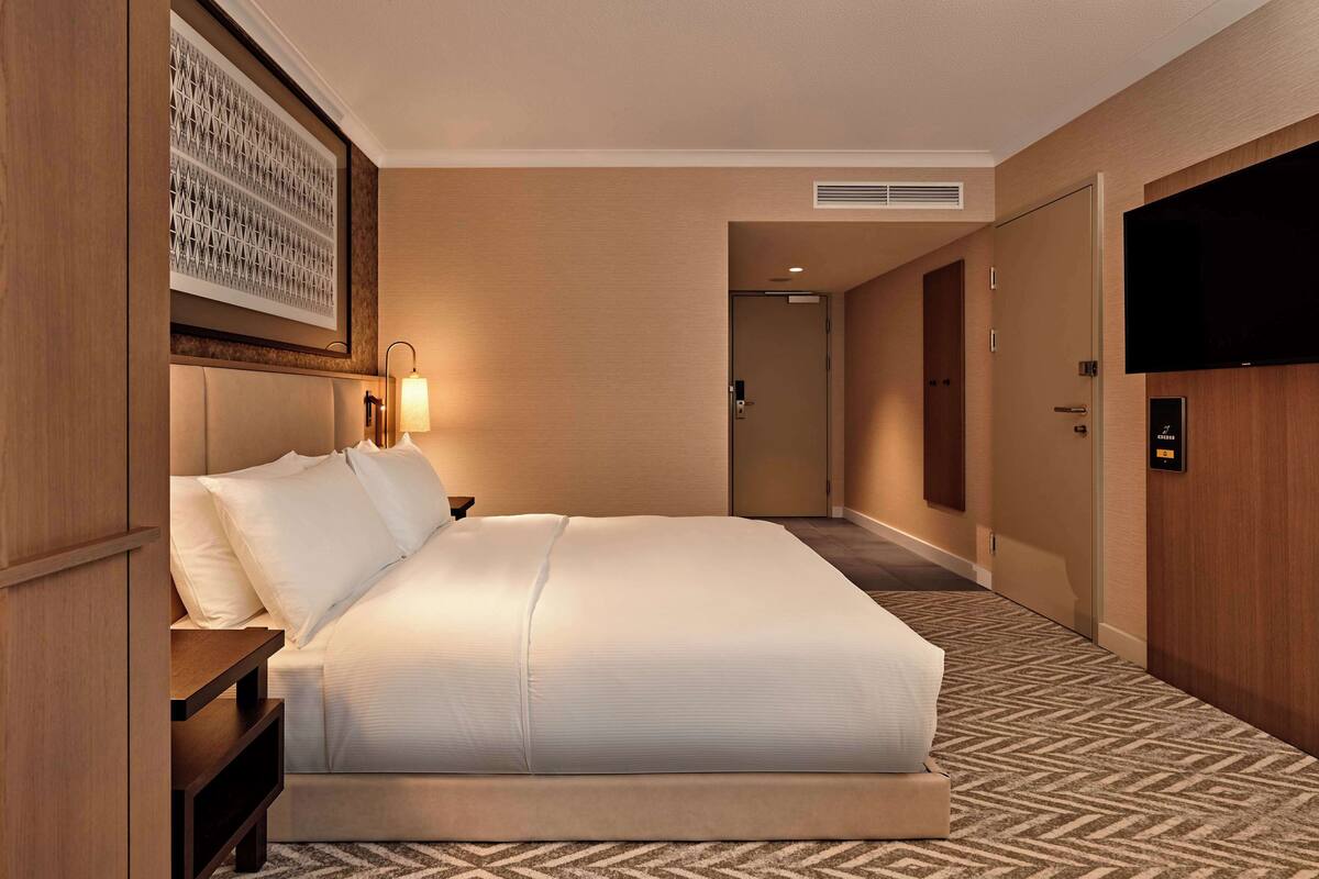 A hotel room with a large bed, a bedside table, a wall-mounted TV, and a framed artwork above the bed.