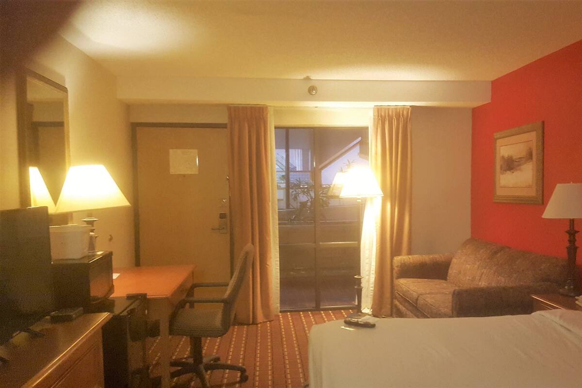 A hotel room with a bed, a desk, a chair, a lamp, and a painting on the wall.