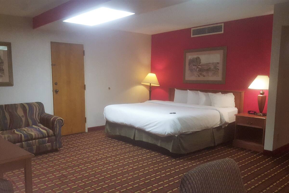 A hotel room with a bed, a chair, a table, and two lamps.