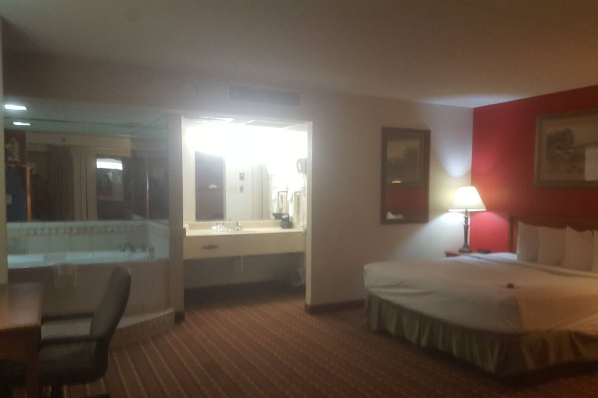 A hotel room with a bed, a desk, a chair, a mirror, a lamp, and a painting on the wall.