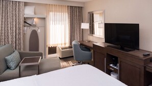 A hotel room with a bed, a desk with a TV, a chair, a desk lamp, a heater, and a window with curtains. - Hampton Inn Los AngelesWest Covina (West Covina)