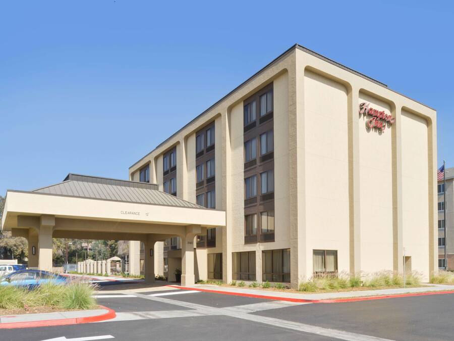 A Hampton Inn hotel with a covered entrance, multiple floors, and a clear blue sky.