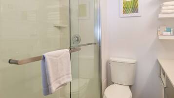 Un baño con cabina de ducha de vidrio, inodoro y toallero con una toalla.