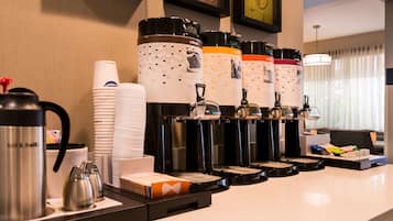 A hotel breakfast bar with multiple coffee dispensers, paper cups, and a kettle.