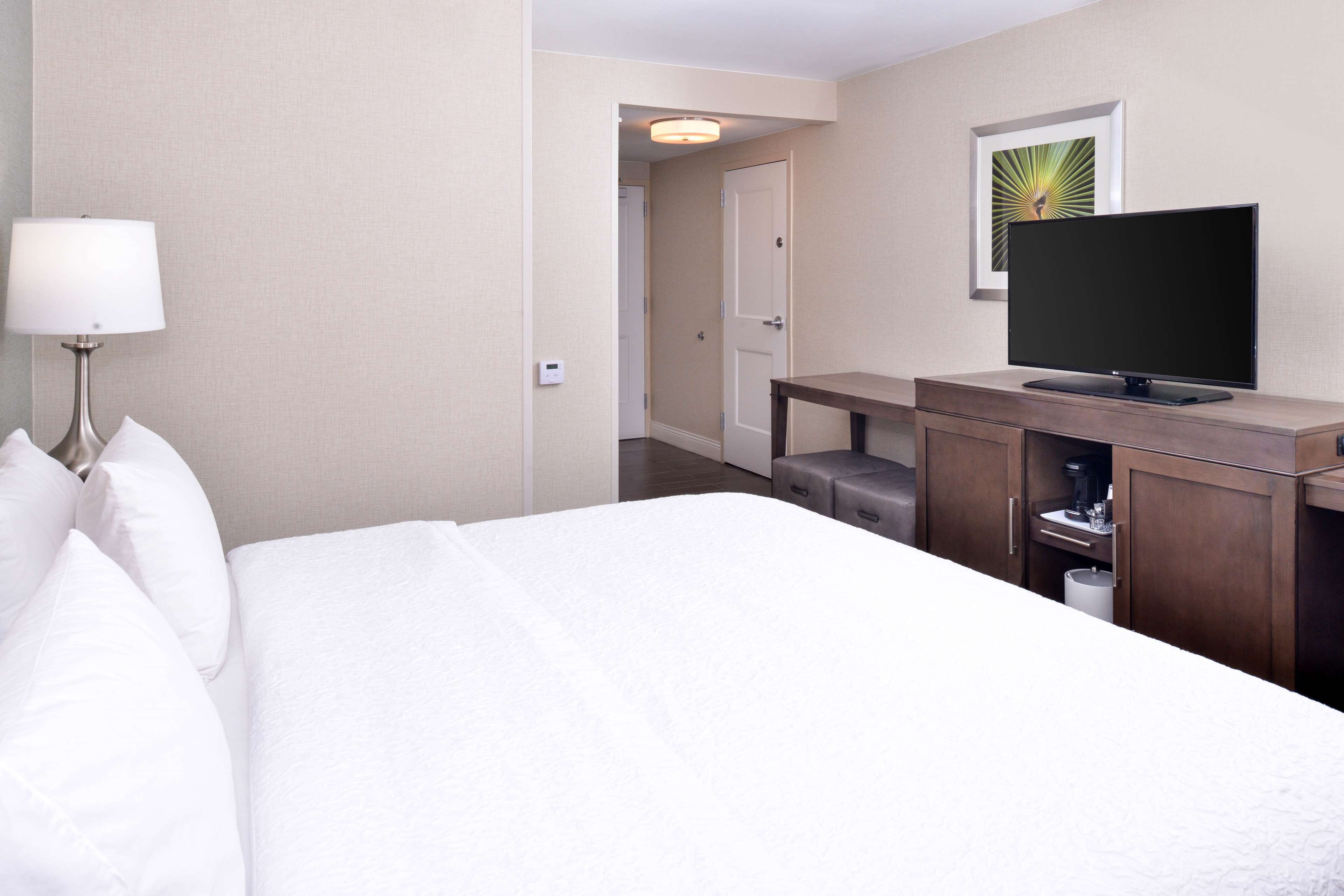 A hotel room with a bed, a TV on a wooden cabinet, a lamp, and a door leading to another room.