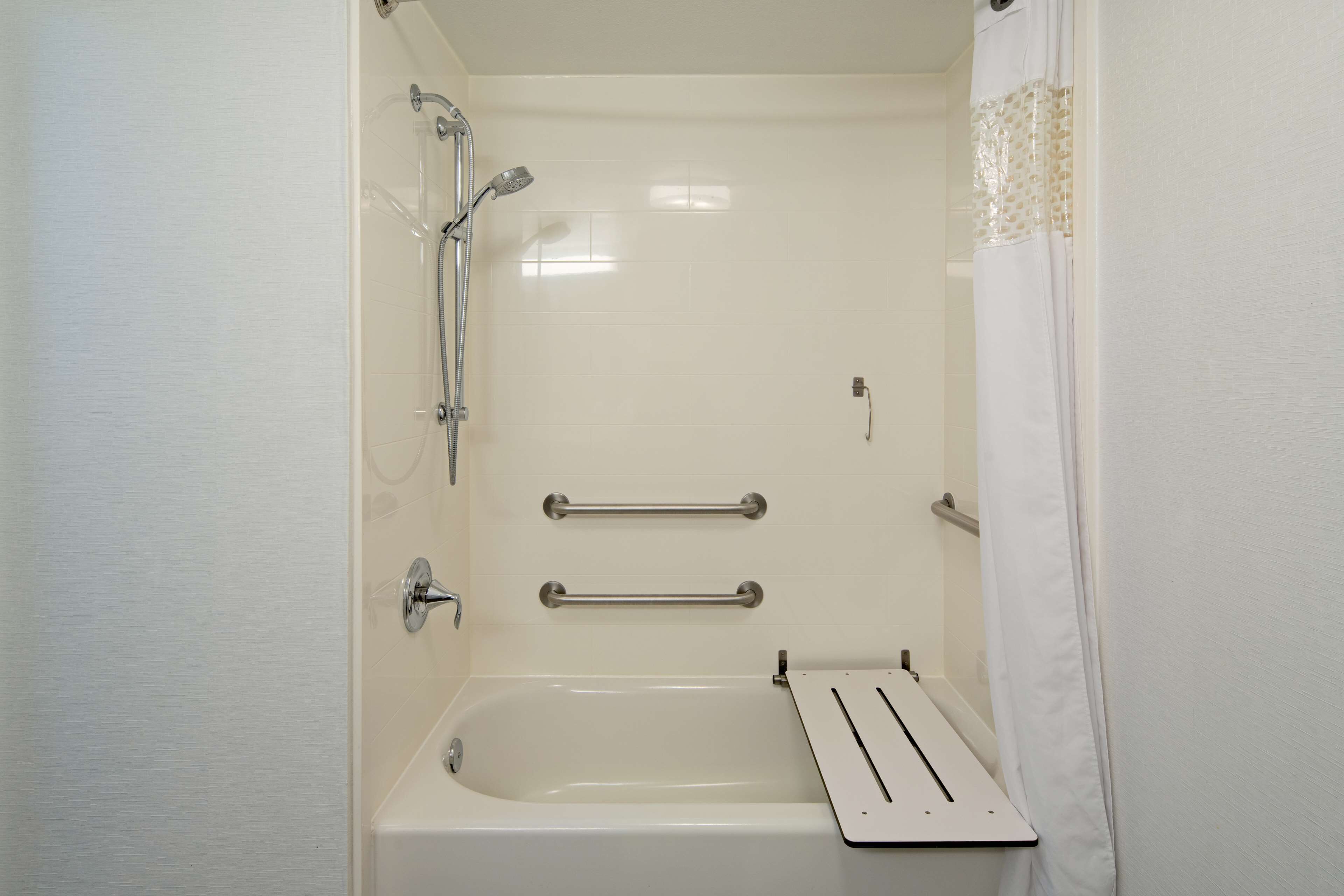 Un baño con bañera, barras de apoyo y ducha.