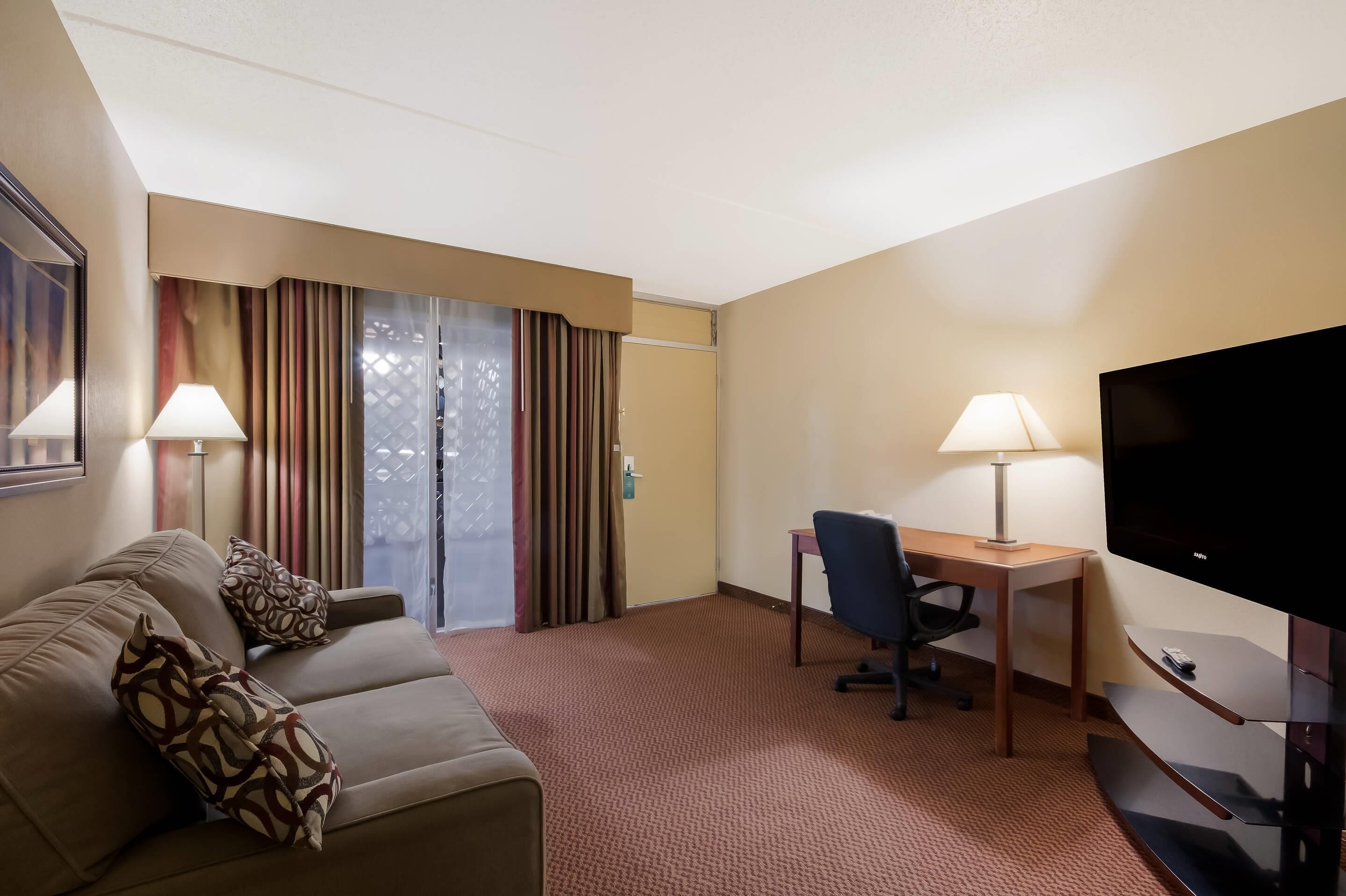 Habitación de hotel con sofá, escritorio, televisor y ventana con cortinas.