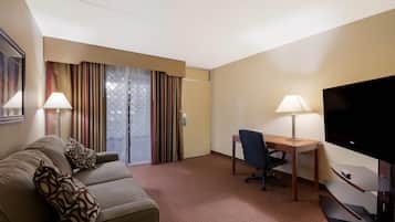 Habitación de hotel con sofá, escritorio, televisor y ventana con cortinas.
