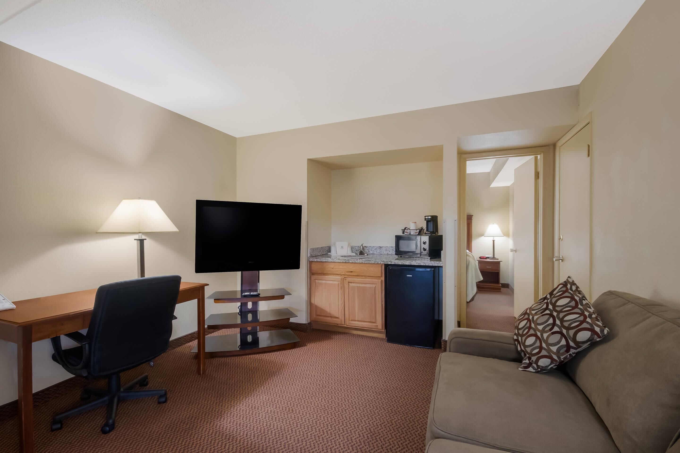 A hotel room with a desk, TV, kitchenette, and a sofa.