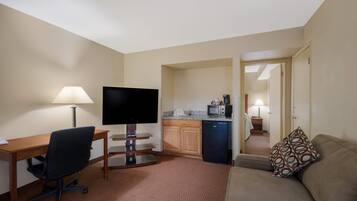 A hotel room with a desk, TV, kitchenette, and a sofa.