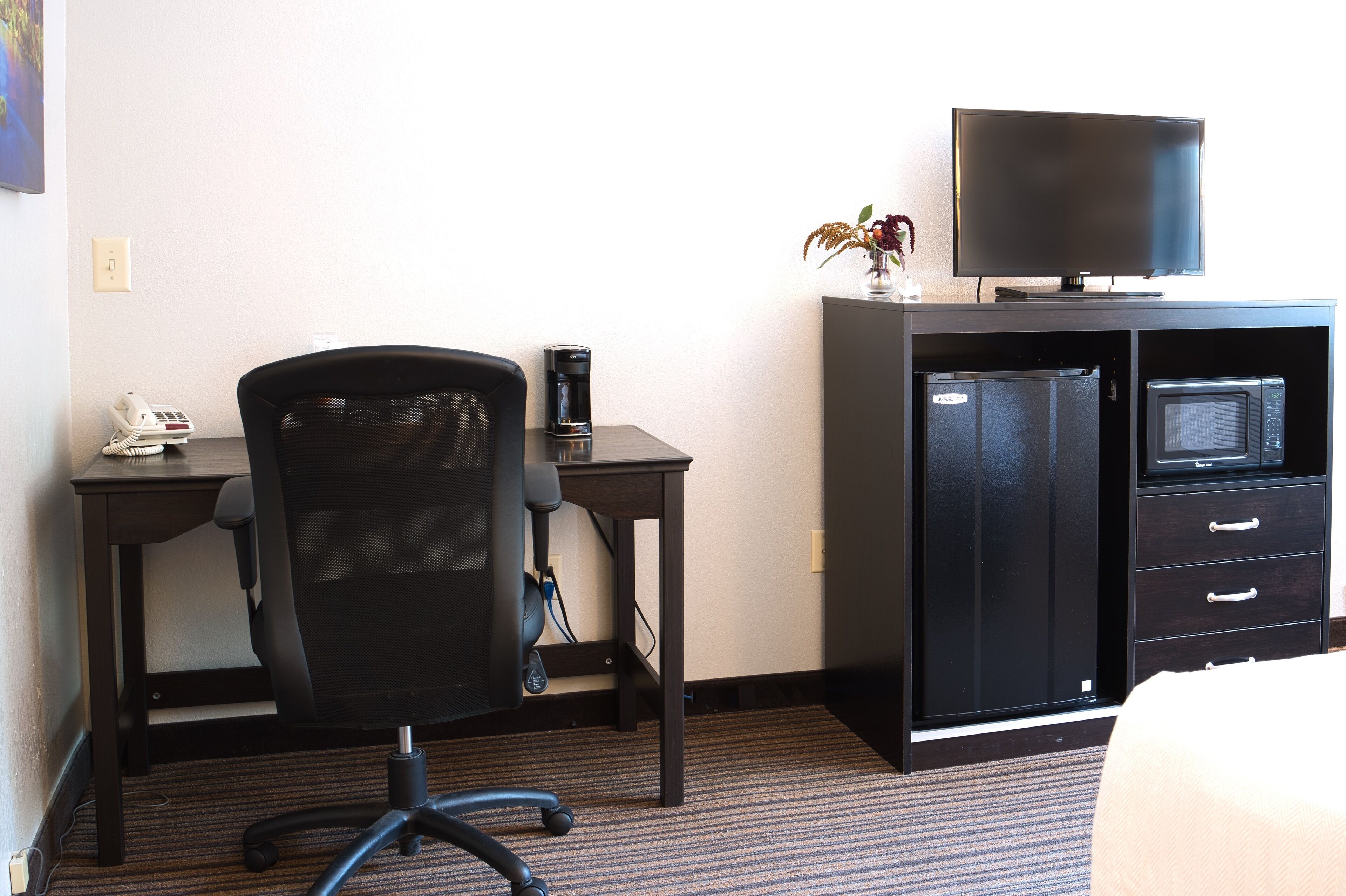 A hotel room with a desk, office chair, coffee maker, television, and a minibar.