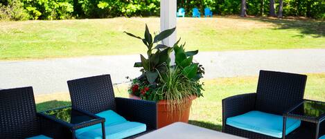 A patio with two wicker chairs and a table, surrounded by greenery and a white structure.