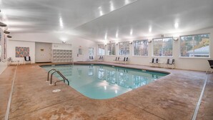 Una piscina interior con agua cristalina, rodeada de sillas de descanso y un suelo de baldosas.