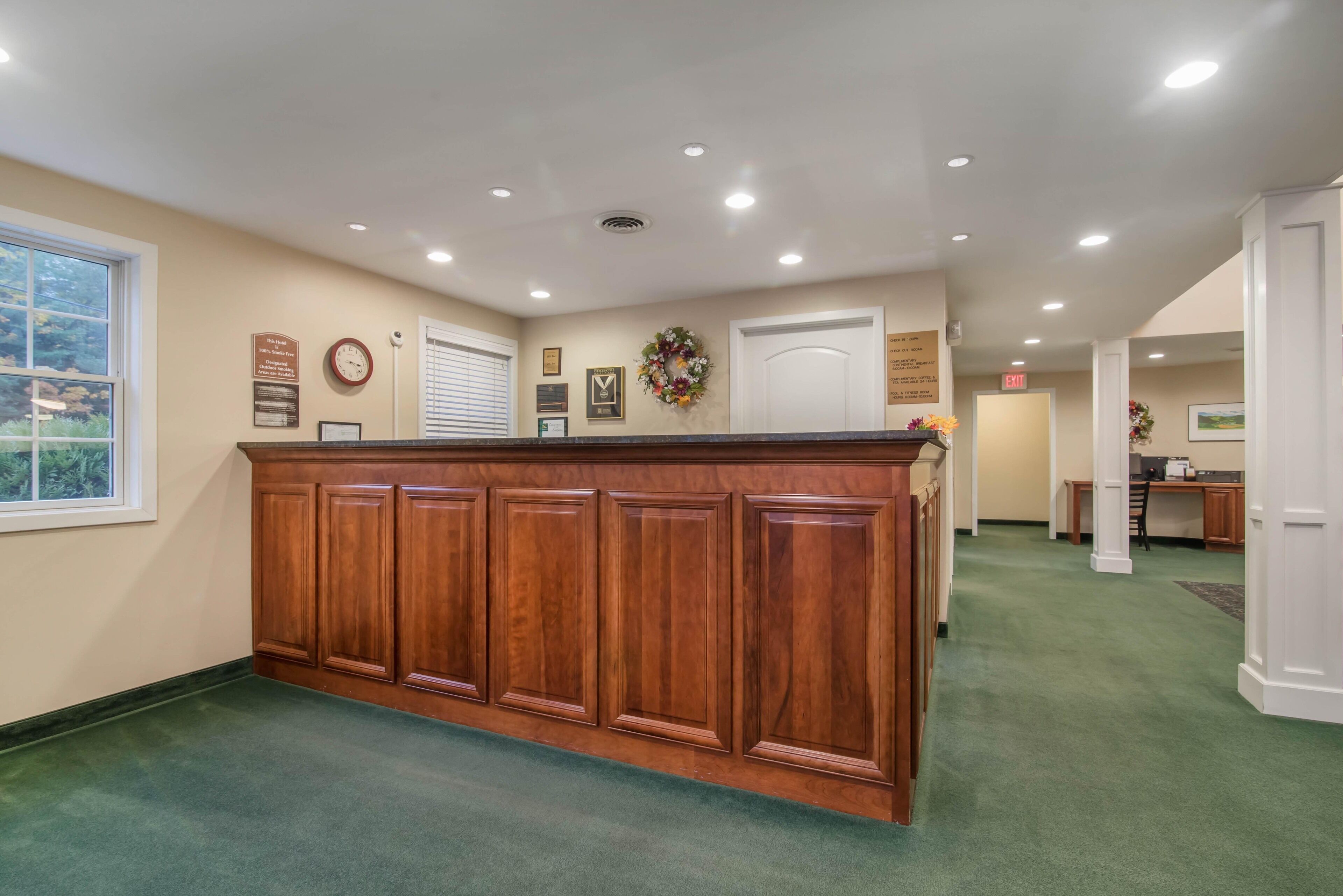 A reception area with a wooden reception desk, beige walls, and a green carpet.