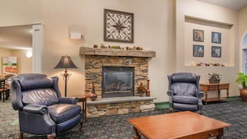 A cozy lounge area with a stone fireplace, leather armchairs, and a wooden coffee table.