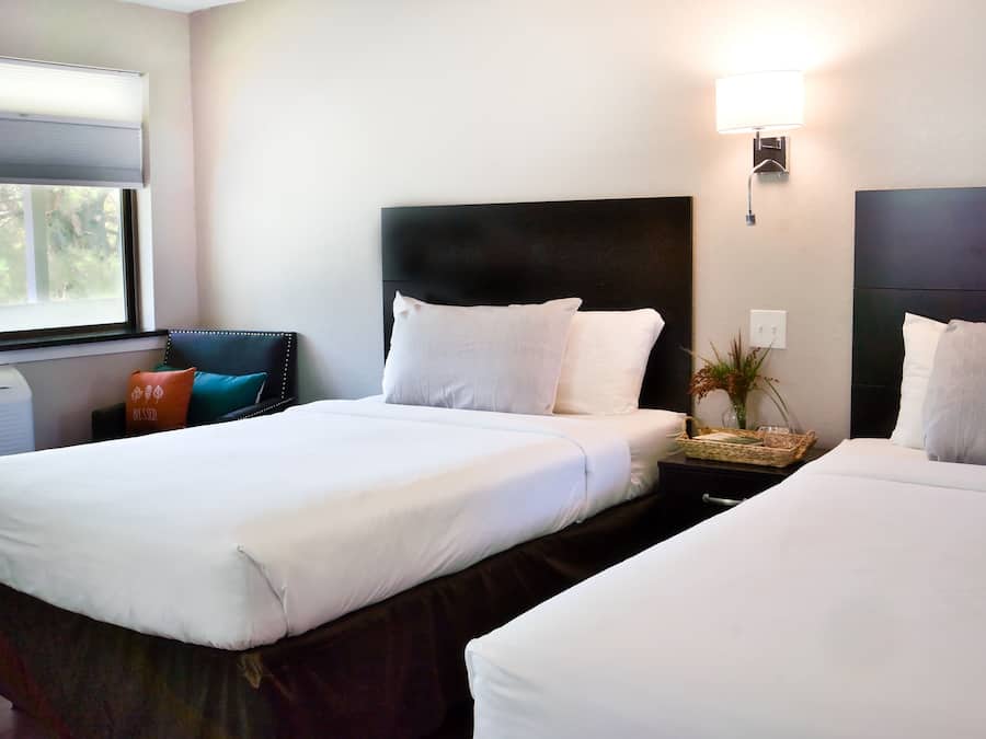 Una habitación de hotel con dos camas, una mesita de noche, una lámpara y una ventana con persianas.