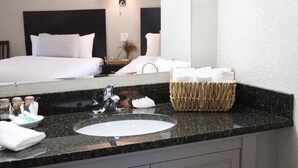 Un baño de hotel con encimera de granito, un lavamanos, un espejo y una cesta de mimbre con toallas.