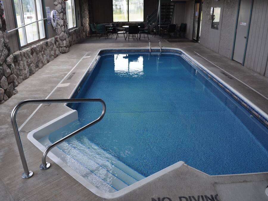 An indoor swimming pool with a stone wall, metal pool ladder, and a 'No Diving' sign.