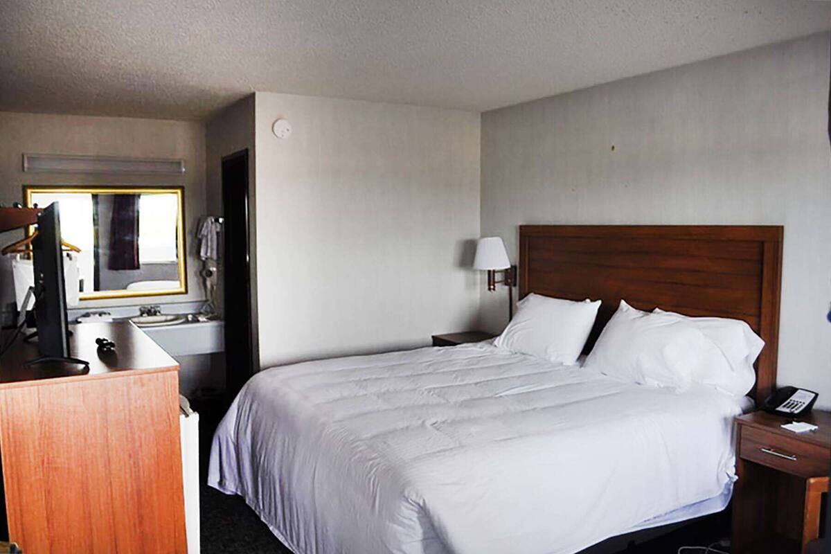 A hotel room with a large bed, a desk with a computer, a mirror, and a lamp.