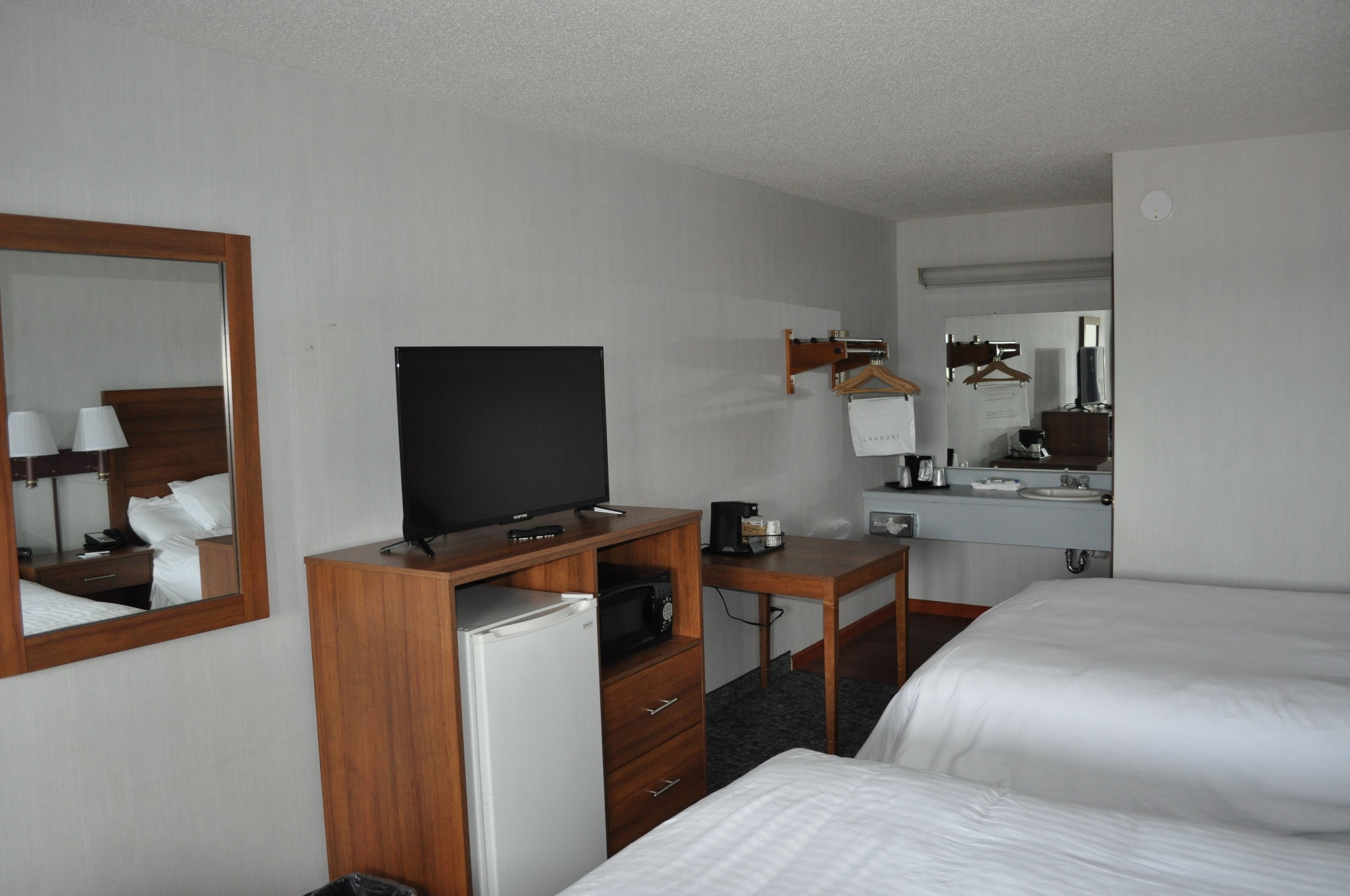 A hotel room with a bed, a desk with a television, a refrigerator, a mirror, and a hanging coat rack.