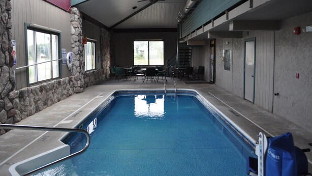 Una piscina interior con paredes de piedra, un ventilador de techo y vistas al exterior a través de amplios ventanales.