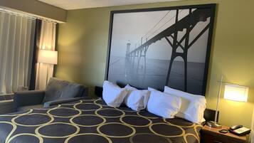 Een hotelkamer met een groot bed, een nachtkastje met een lamp, een stoel en een muur met een groot beeld van een brug.
