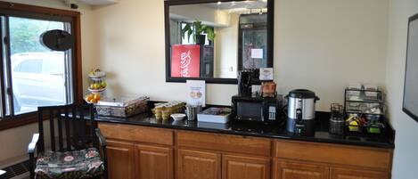A kitchen with wooden cabinets, a black countertop, a microwave, a coffee maker, and a potted plant.