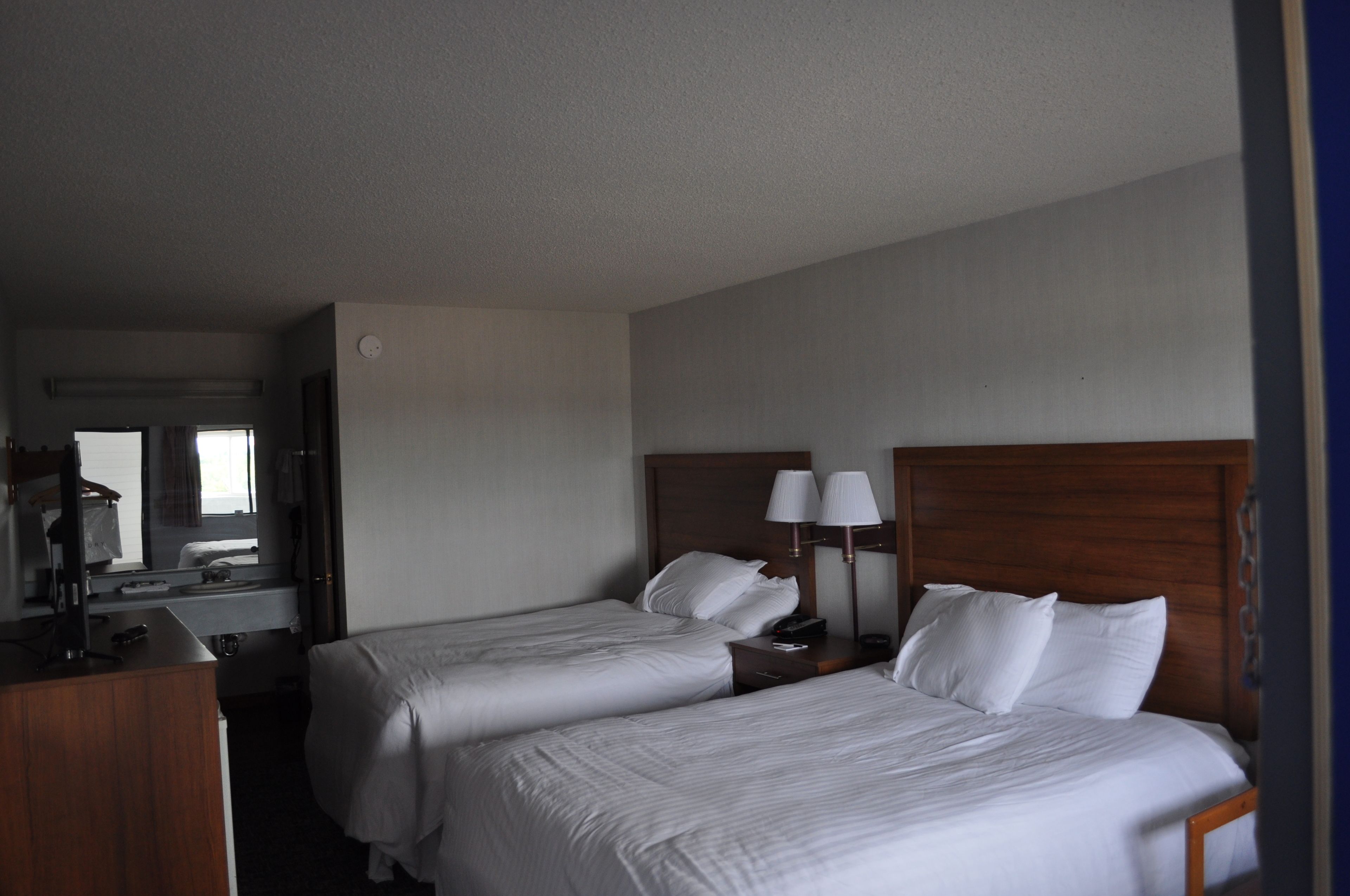 A hotel room with two single beds, a wooden headboard, a desk with a mirror, and a nightstand with lamps.