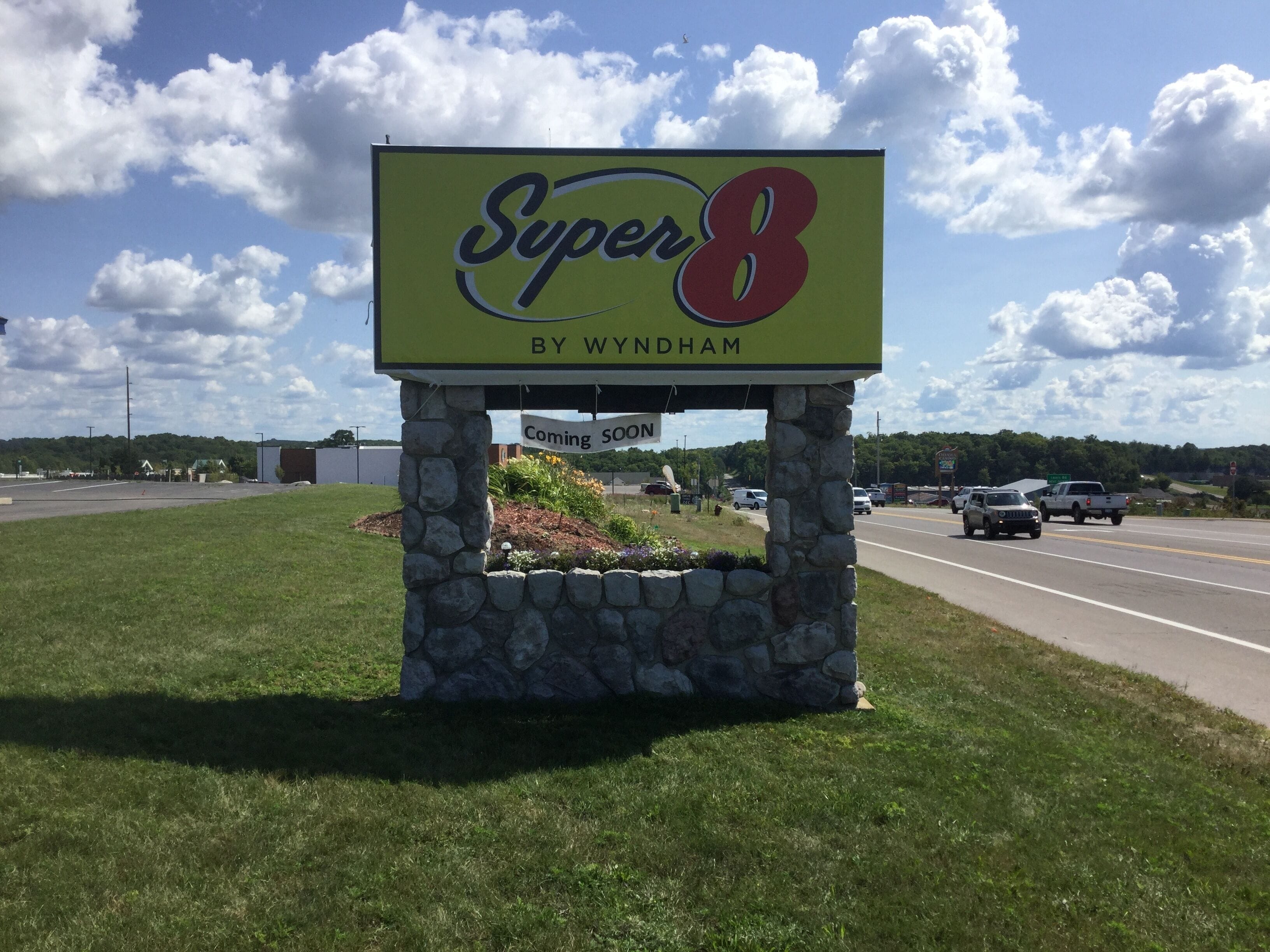 A Super 8 by Wyndham sign with a 'Coming Soon' message, set against a backdrop of a road and a clear sky.