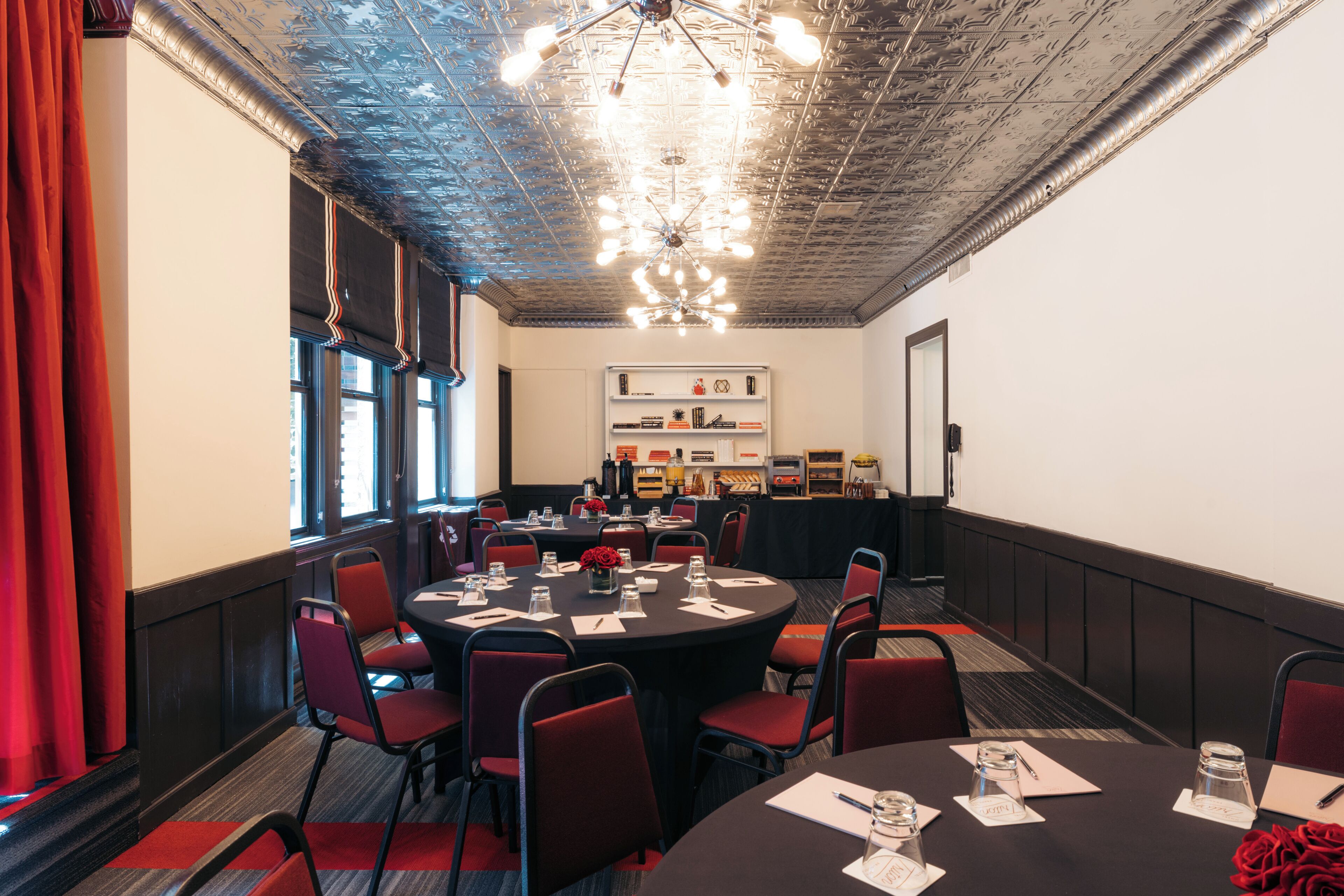 A conference room with a round table, red chairs, a chandelier, and a bookshelf in the background.