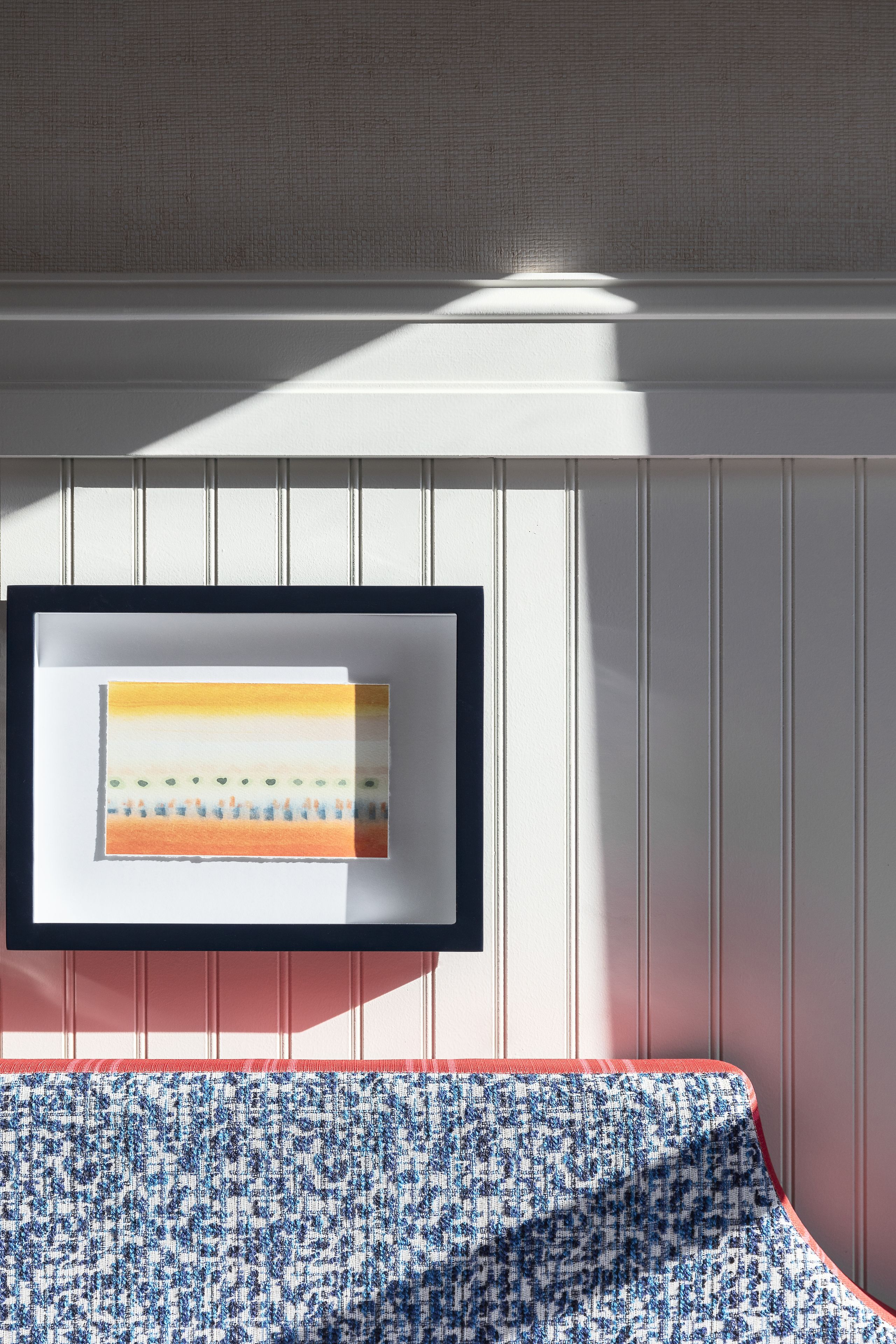 A room with a framed artwork on the wall, a patterned sofa, and vertical paneling.