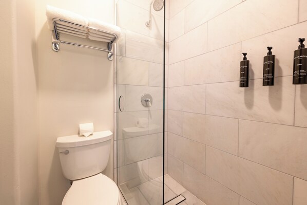 Un baño moderno con cabina de ducha de vidrio, un inodoro blanco y tres artículos de tocador montados en la pared.