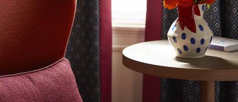 A red chair, a white vase with blue polka dots, and a patterned curtain in a room.