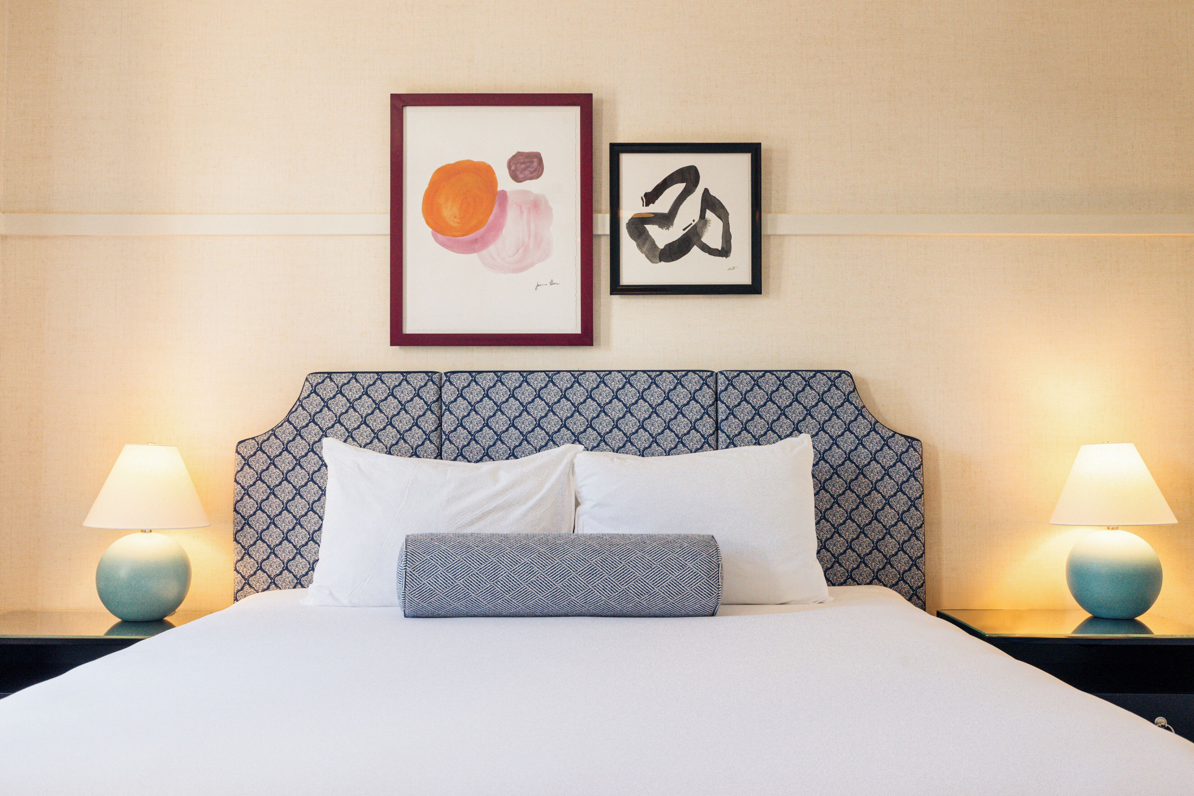 A neatly made bed with white linens, two pillows, and a patterned pillow. There are two wall-mounted lamps on either side of the bed.